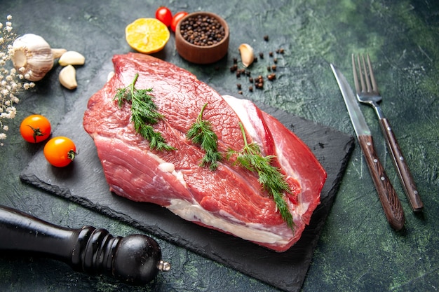 Vista laterale del verde su carne cruda rossa fresca su tagliere e fiore di martello nero limone pepe su sfondo nero verde mix di colore