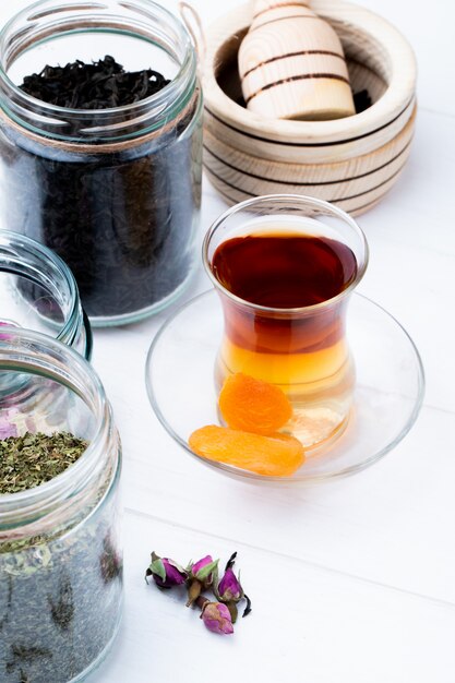 Vista laterale del vetro di armudu di tè con le varie spezie ed erbe in barattoli di vetro su bianco