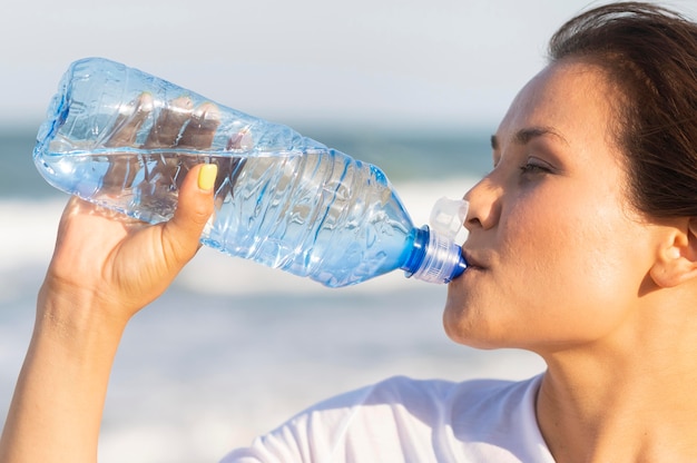 Vista laterale dell'acqua potabile della donna sulla spiaggia dopo l'esercizio