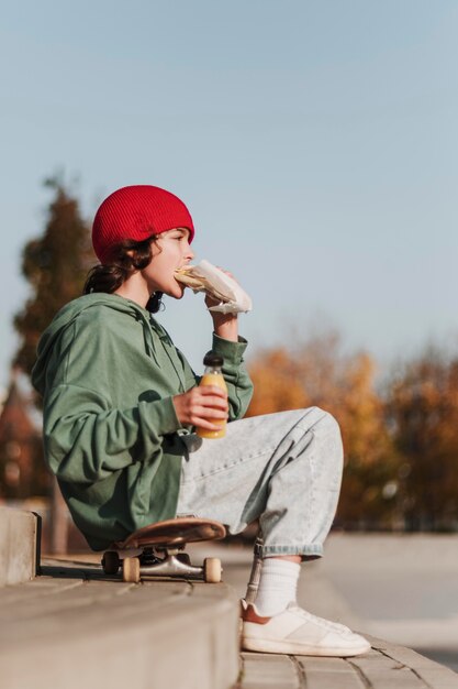 Vista laterale dell'adolescente a pranzo sullo skateboard