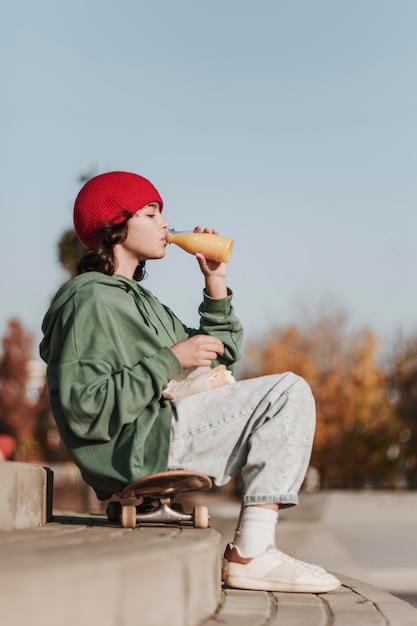 Vista laterale dell'adolescente che mangia succo il parco su skateboard