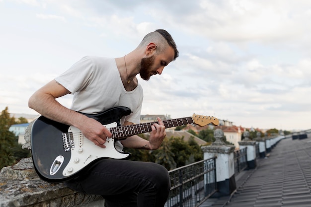 Vista laterale dell'artista maschio sul tetto a suonare la chitarra elettrica