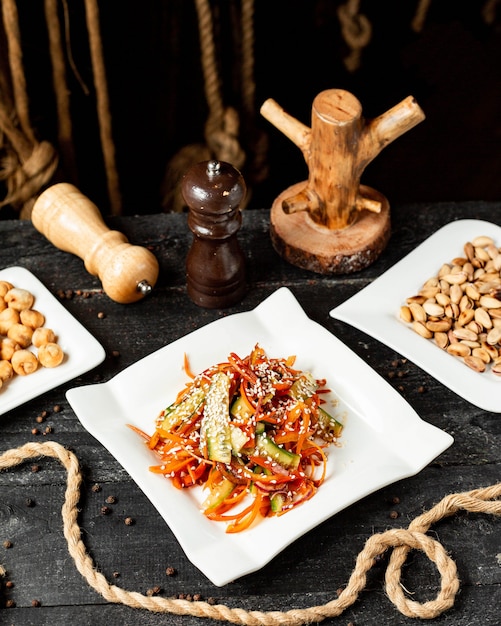 Vista laterale dell'insalata di carota con i peperoni e il sesamo dei cetrioli sul piatto