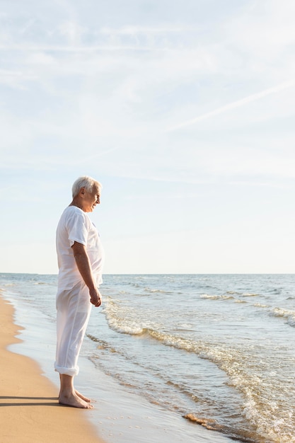 Vista laterale dell'uomo anziano che riposa mentre ammira la vista della spiaggia