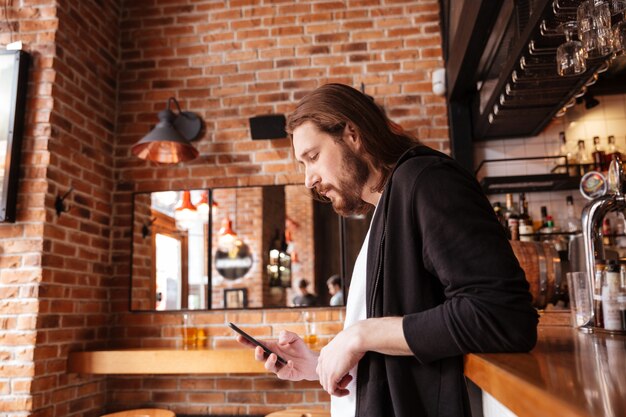 Vista laterale dell'uomo che sta sulla barra con il telefono