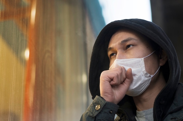 Vista laterale dell'uomo che tossisce mentre indossa una maschera medica