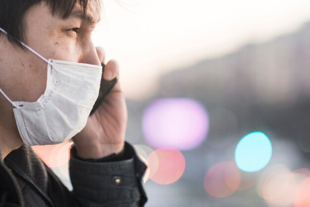 Vista laterale dell'uomo con la mascherina medica che comunica sul telefono