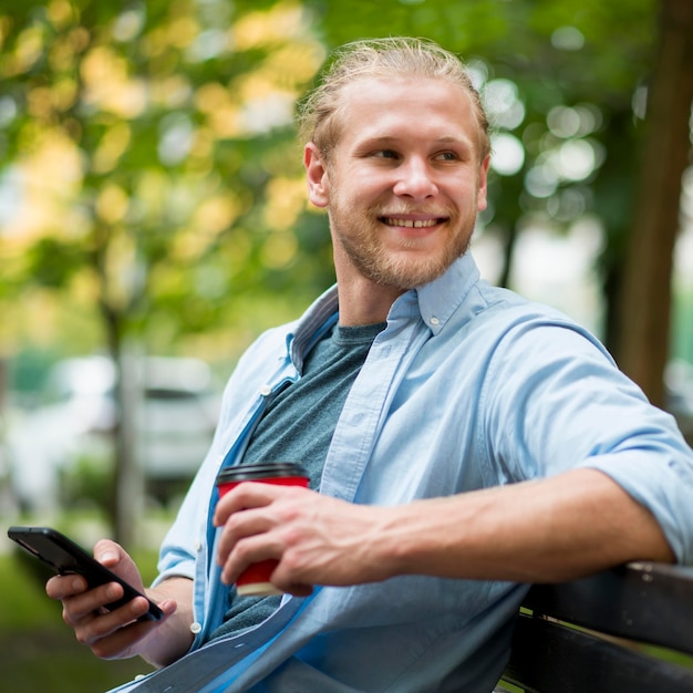 Vista laterale dell'uomo di smiley all'aperto con lo smartphone e la tazza