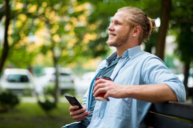 Vista laterale dell'uomo di smiley all'aperto con lo smartphone