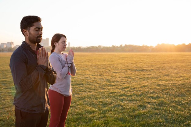 Vista laterale dell'uomo e della donna che fanno yoga insieme all'aperto