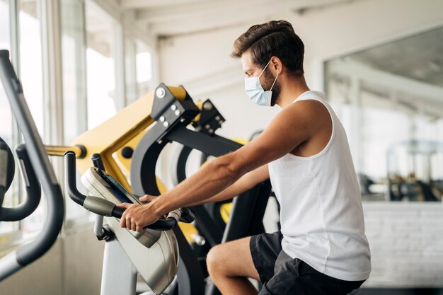 Vista laterale dell'uomo in palestra lavorando con mascherina medica