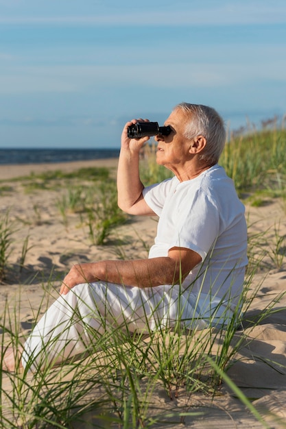 Vista laterale dell'uomo più anziano con il binocolo ammirando la spiaggia
