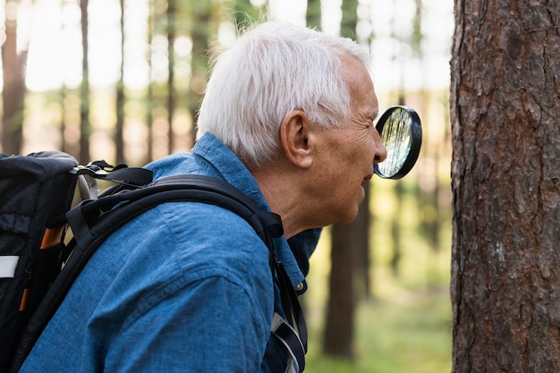 Vista laterale dell'uomo più anziano in natura con lente d'ingrandimento