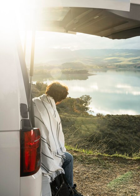 Vista laterale dell'uomo seduto sul bagagliaio dell'auto durante un viaggio su strada