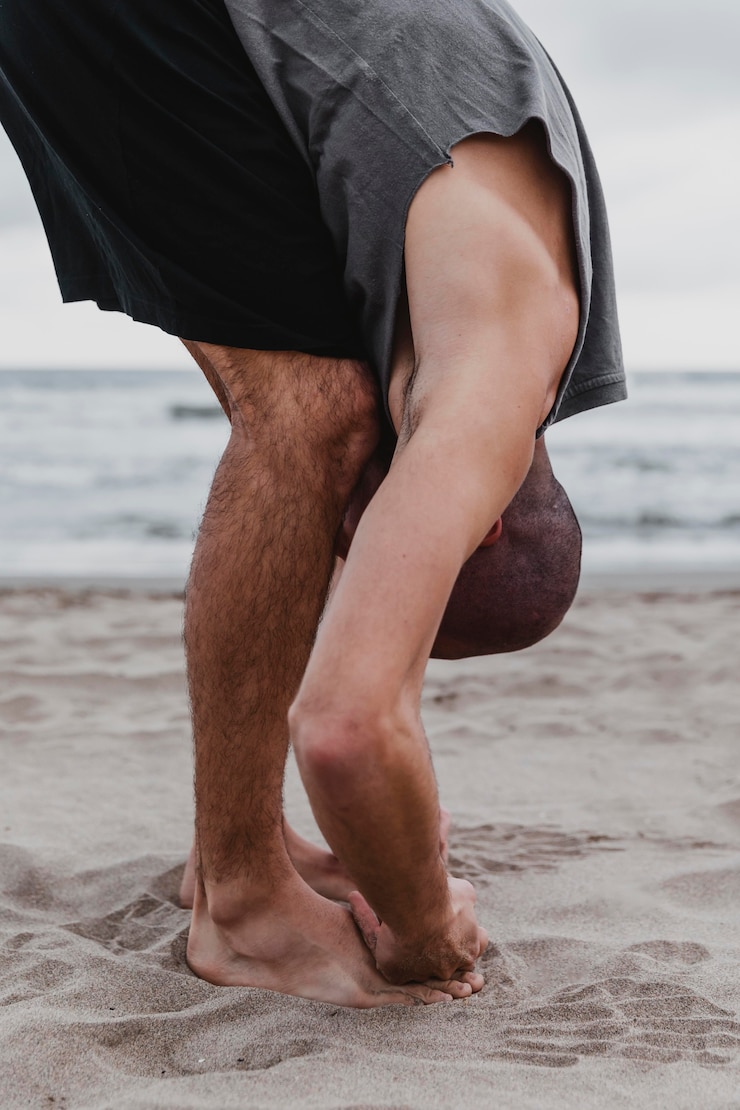 Foto gratuito vista laterale dell'uomo sulla spiaggia che esercita posizioni yoga sulla sabbia