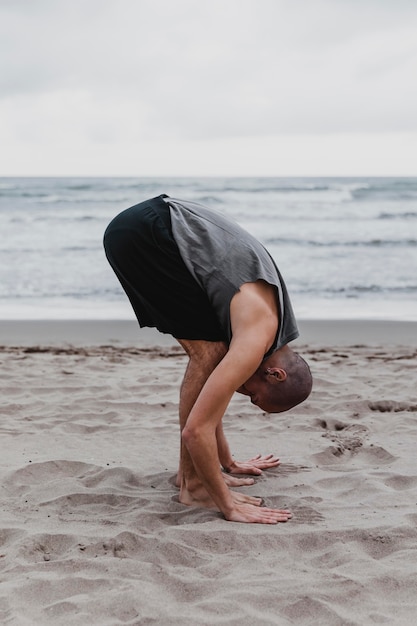 Vista laterale dell'uomo sulla spiaggia che esercita posizioni yoga