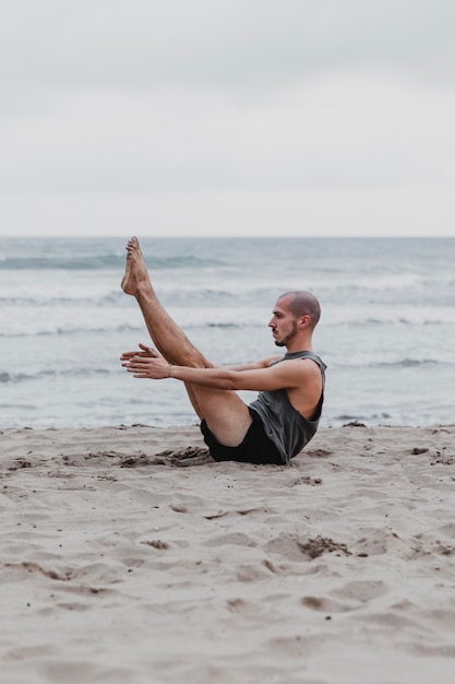 Vista laterale dell'uomo sulla spiaggia in posizione yoga con copia spazio