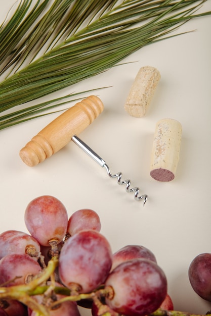 Vista laterale dell'uva dolce fresca con la vite della bottiglia e sugheri di un vino sulla tavola bianca