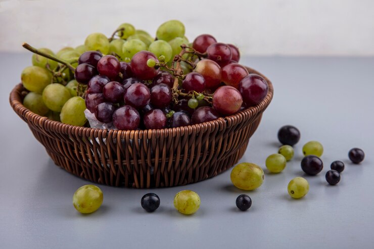 Foto gratuito vista laterale dell'uva nel cesto e modello di acini d'uva su superficie grigia e sfondo bianco