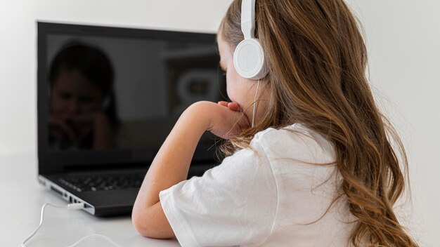 Vista laterale della bambina utilizzando laptop con le cuffie