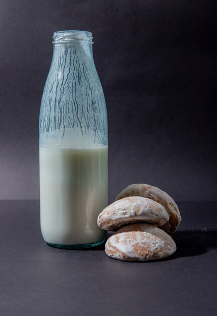 Vista laterale della bottiglia di latte e dei biscotti sulla superficie del nero