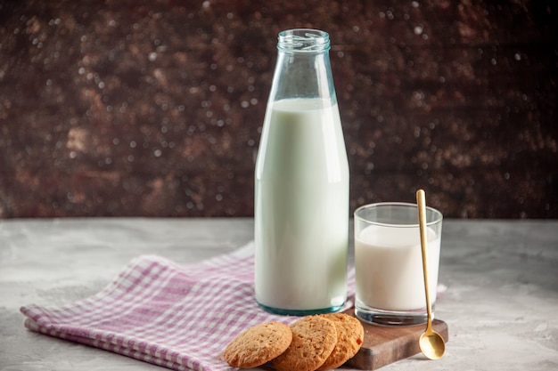 Vista laterale della bottiglia di vetro aperta e della tazza piena di biscotti al latte su un asciugamano spogliato viola su tagliere di legno
