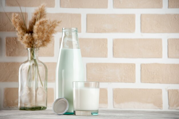 Vista laterale della bottiglia di vetro e della tazza riempita con tappo per il latte sul lato destro su sfondo di mattoni di colore pastello