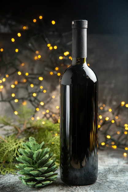Vista laterale della bottiglia di vino rosso per la celebrazione e un cono di conifera verde su sfondo scuro