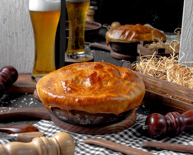 Vista laterale della casseruola con le salsiccie in una ciotola dell'argilla su un tagliere di legno