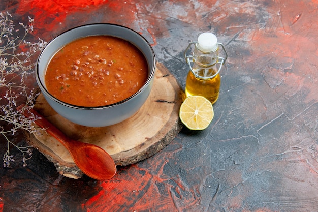 Vista laterale della classica zuppa di pomodoro in una ciotola blu sulla bottiglia di olio vassoio di legno e limone sulla tabella di colori misti