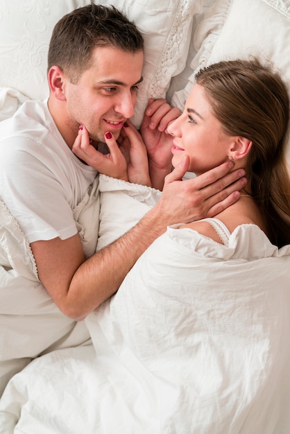 Vista laterale della coppia abbracciata nel letto a letto e guardarsi