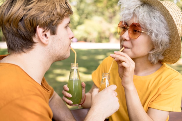 Vista laterale della coppia carina bere succo di frutta nel parco con cannucce