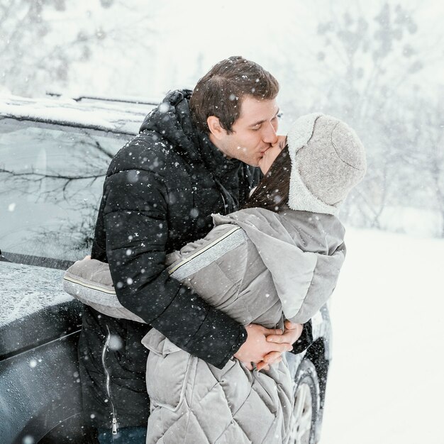 Vista laterale della coppia che si bacia nella neve durante un viaggio su strada