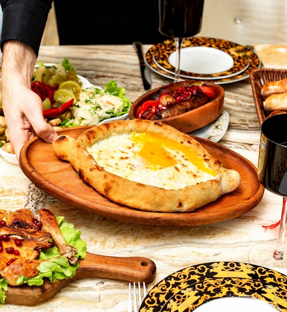 Vista laterale della cucina georgiana tradizionale khachapuri adjara con ripieno di uova e formaggio sul piatto di legno