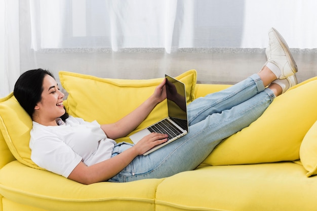 Vista laterale della donna a casa sul divano con il computer portatile