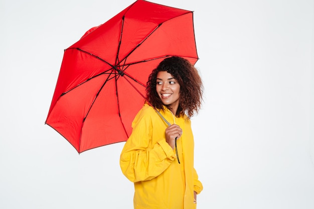 Vista laterale della donna africana sorridente nella posa dell'impermeabile