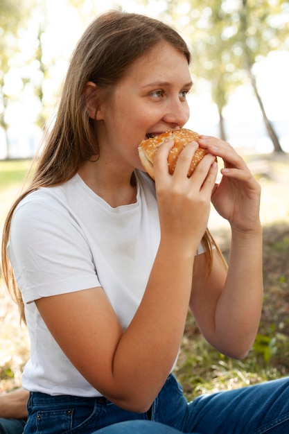 Vista laterale della donna al parco che mangia hamburger