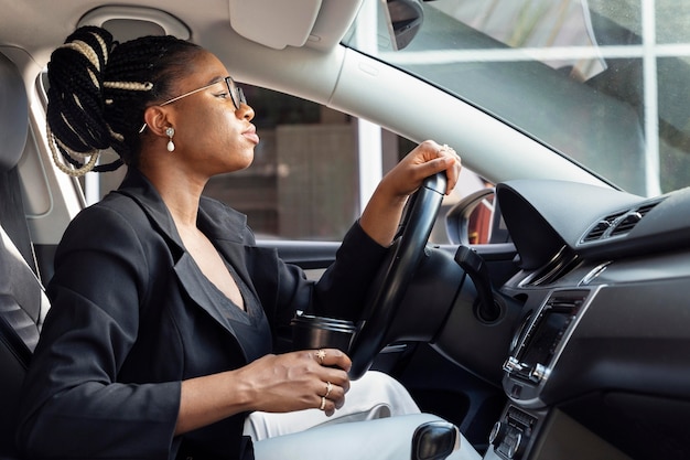 Vista laterale della donna alla guida di auto tenendo la tazza di caffè