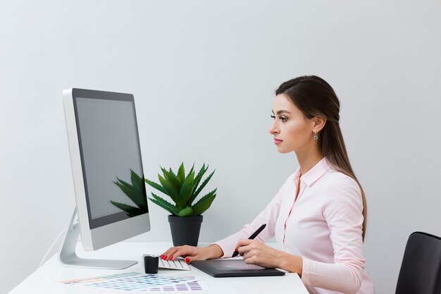 Vista laterale della donna allo scrittorio che lavora con il suo tablet