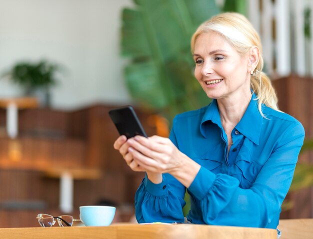 Vista laterale della donna anziana che tiene smartphone mentre si lavora