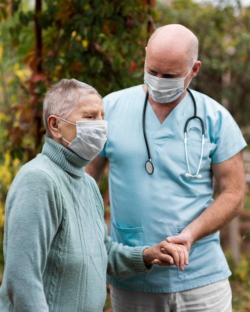 Vista laterale della donna anziana con maschera medica e infermiere maschio