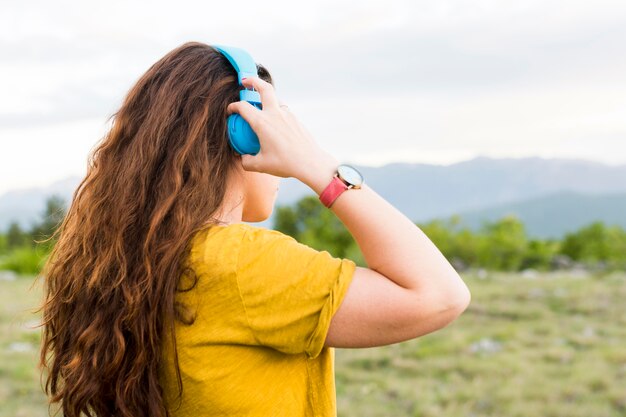 Vista laterale della donna che ascolta la musica sulle cuffie in natura