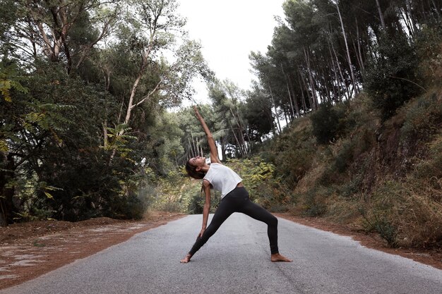 Vista laterale della donna che fa yoga sulla strada in natura