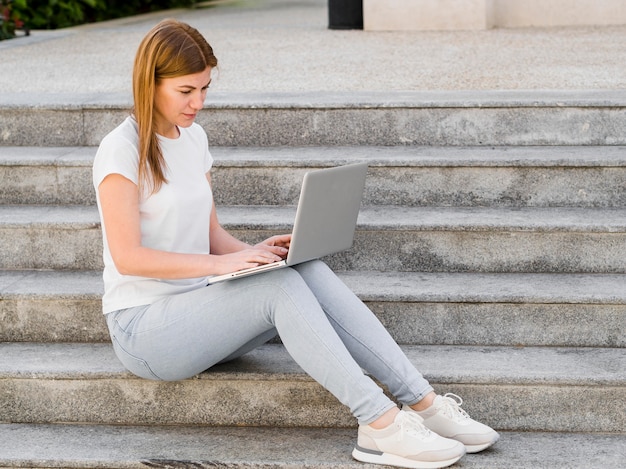 Vista laterale della donna che lavora al computer portatile all'aperto sui punti