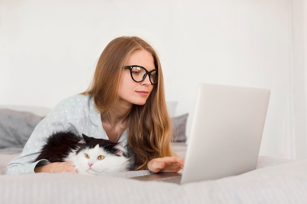 Vista laterale della donna che lavora al computer portatile da casa in pigiama con il gatto