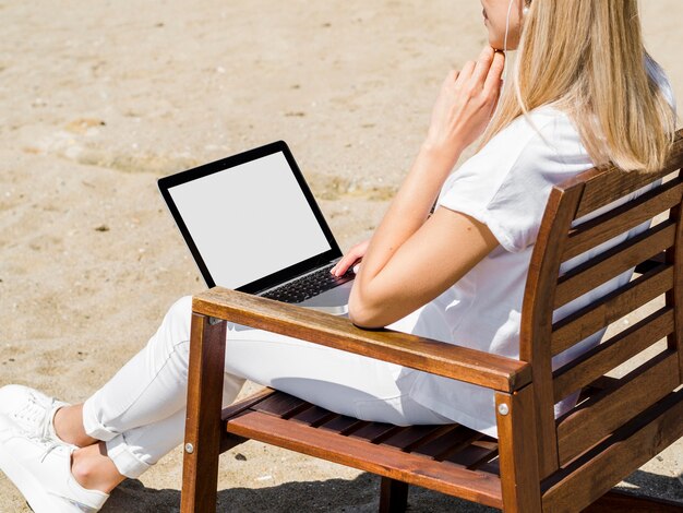 Vista laterale della donna che lavora al computer portatile nella sedia di spiaggia