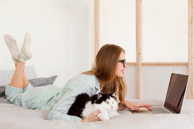 Vista laterale della donna che lavora in pigiama da casa con il gatto