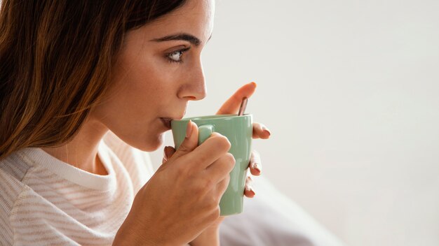 Vista laterale della donna che mangia il caffè a letto con lo spazio della copia