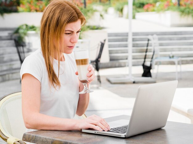 Vista laterale della donna che mangia latte e che lavora al computer portatile