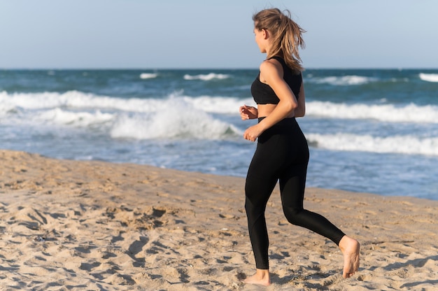 Vista laterale della donna che pareggia sulla spiaggia